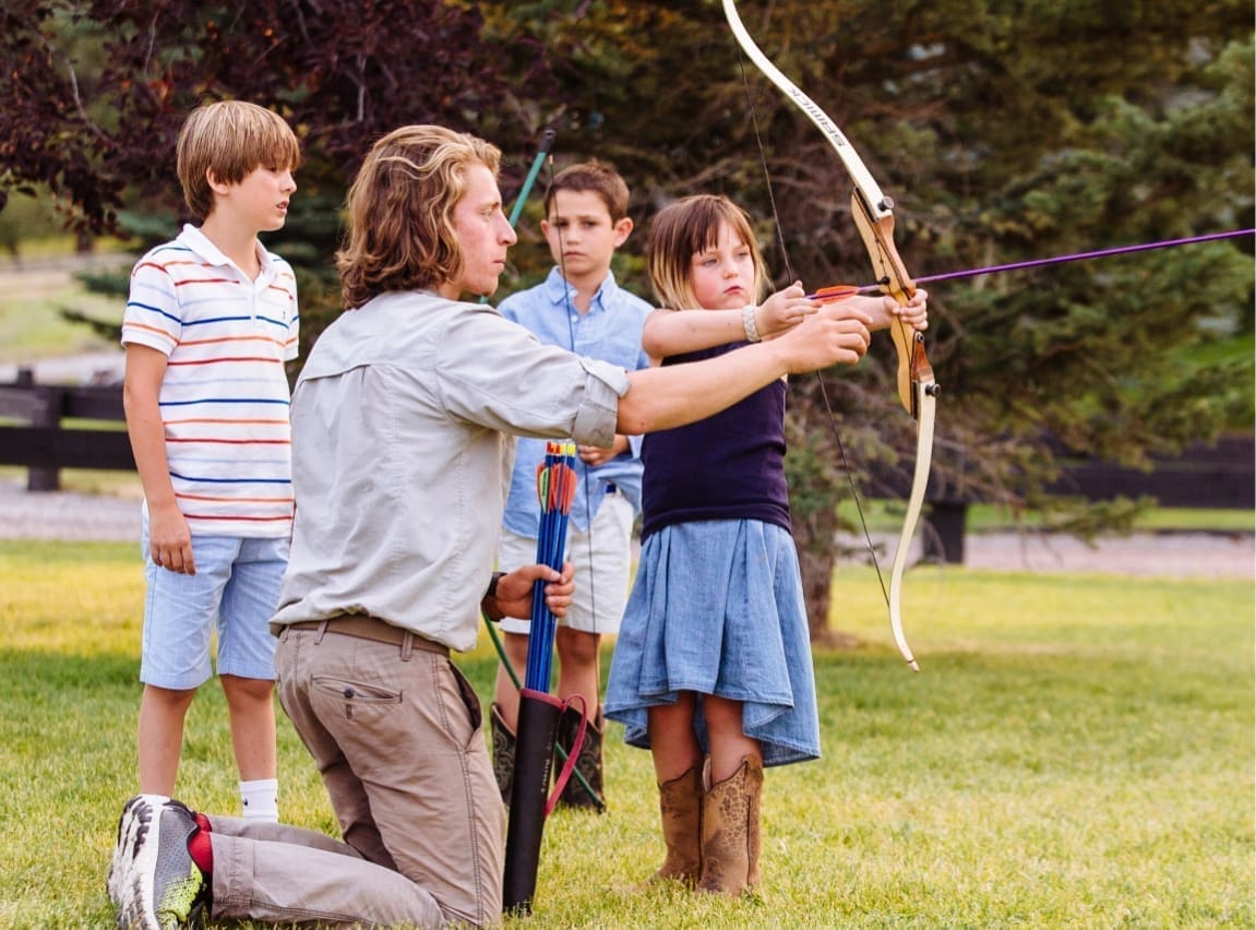 man instructing children to shoot a bow and arrow for archery