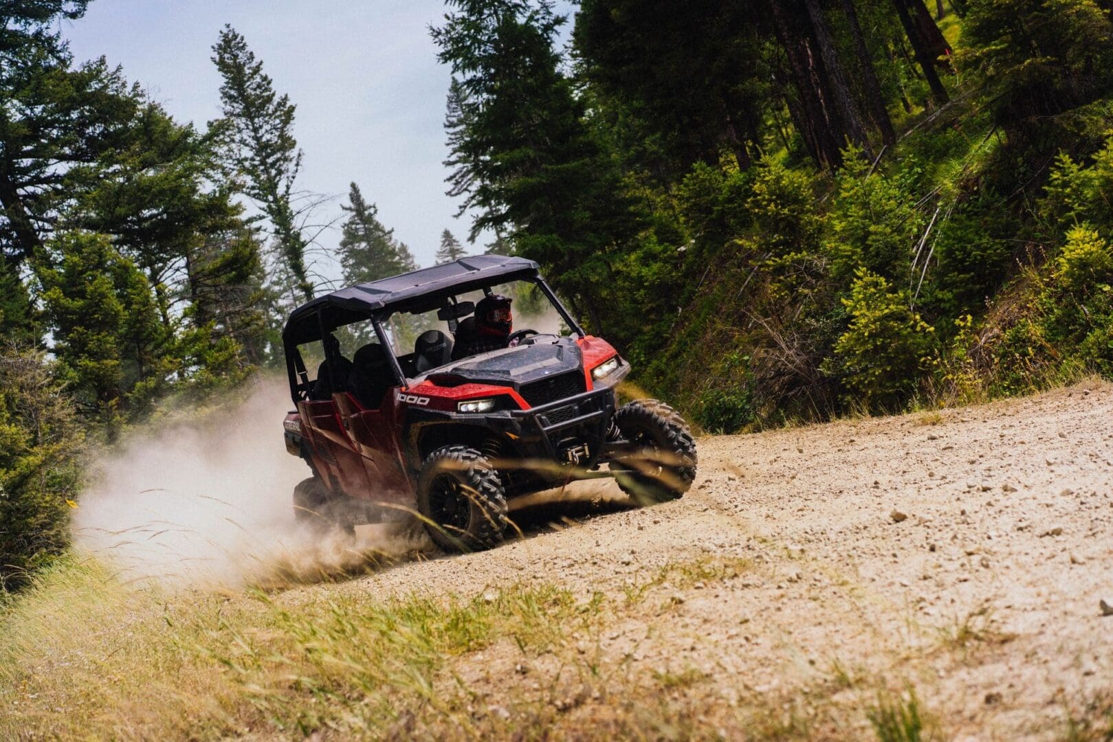 A red Polaris UTV sliding through the dust on a mountain dirt road