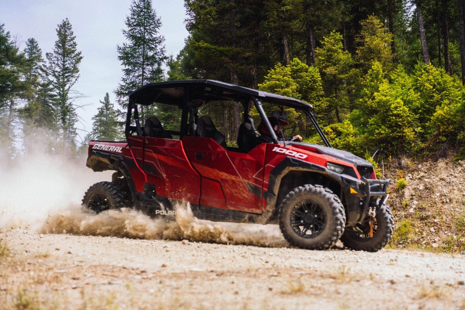 A red Polaris UTV gliding through the dirt on a mountain road