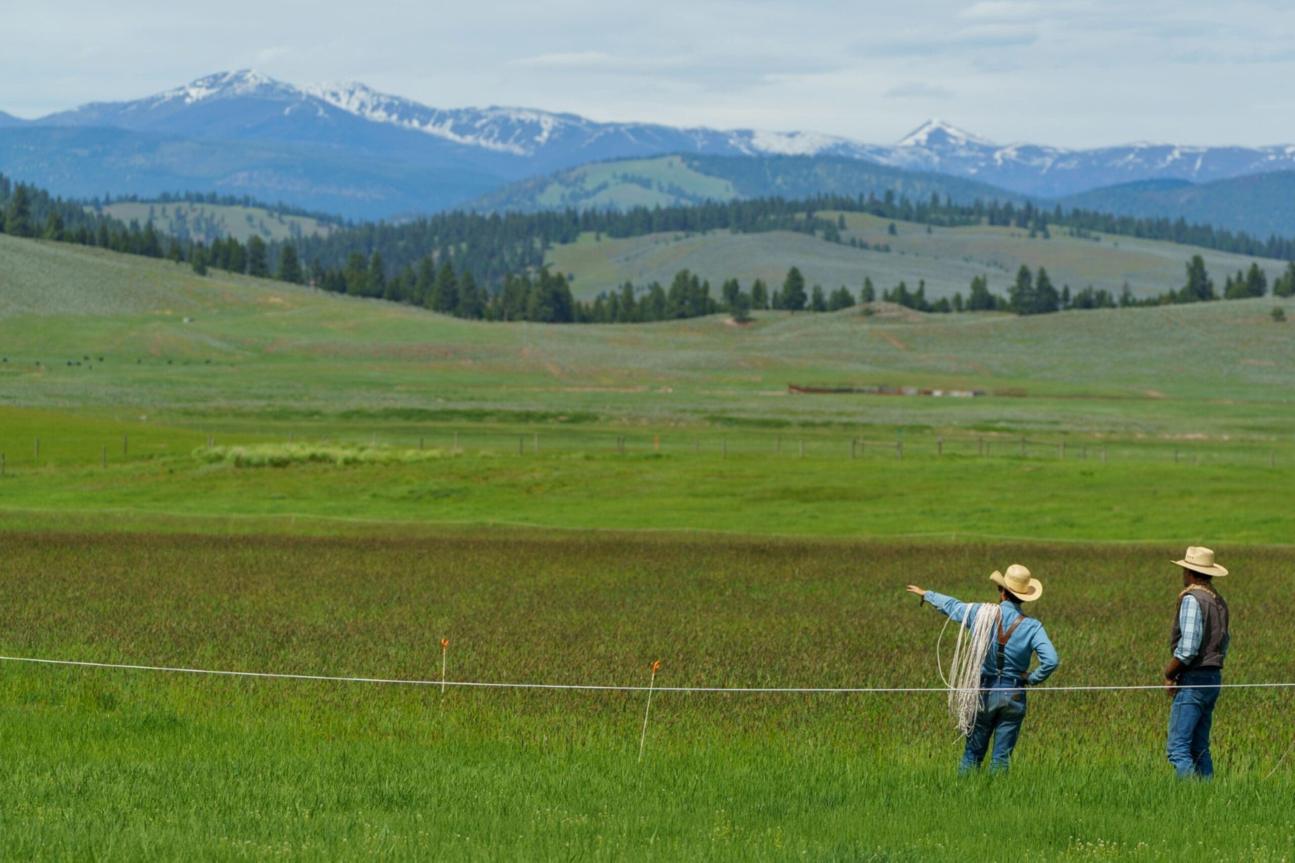 Two ranch workers roping out the land in a Montana mountain summer valley