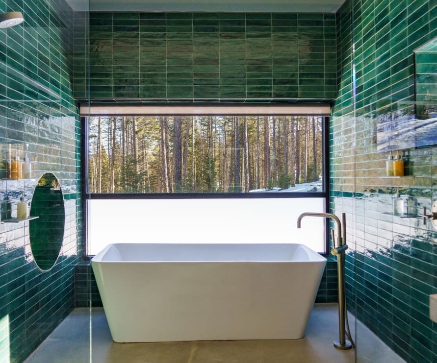 Inside view of the Green Haus bathroom, a dark green-tiled shower with a bathtub and view of the forest from a window