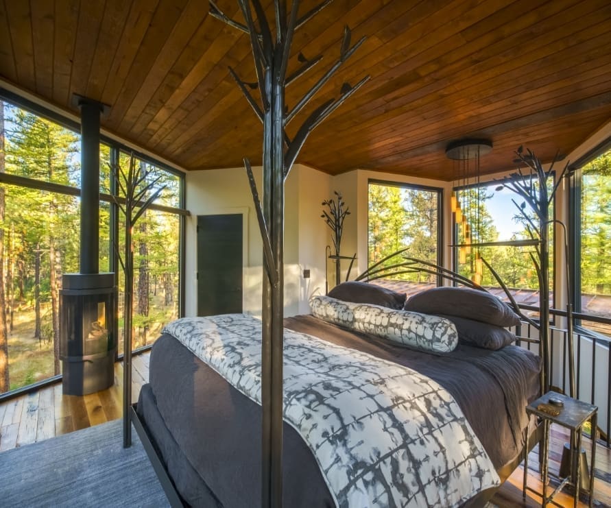 Bedroom in Tree Haus in Green O, a king size bed with a dark gray comforter and surrounded by windows