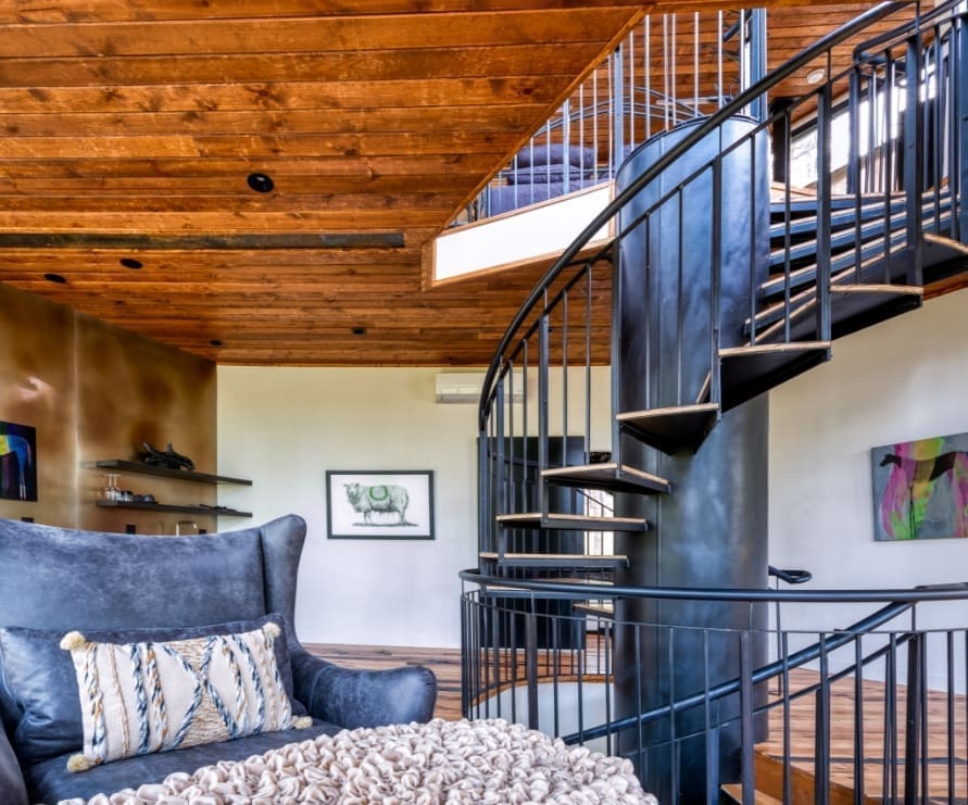 Inside view of Tree Haus showcasing the living room with a leather chair and spiral metal staircase through the middle