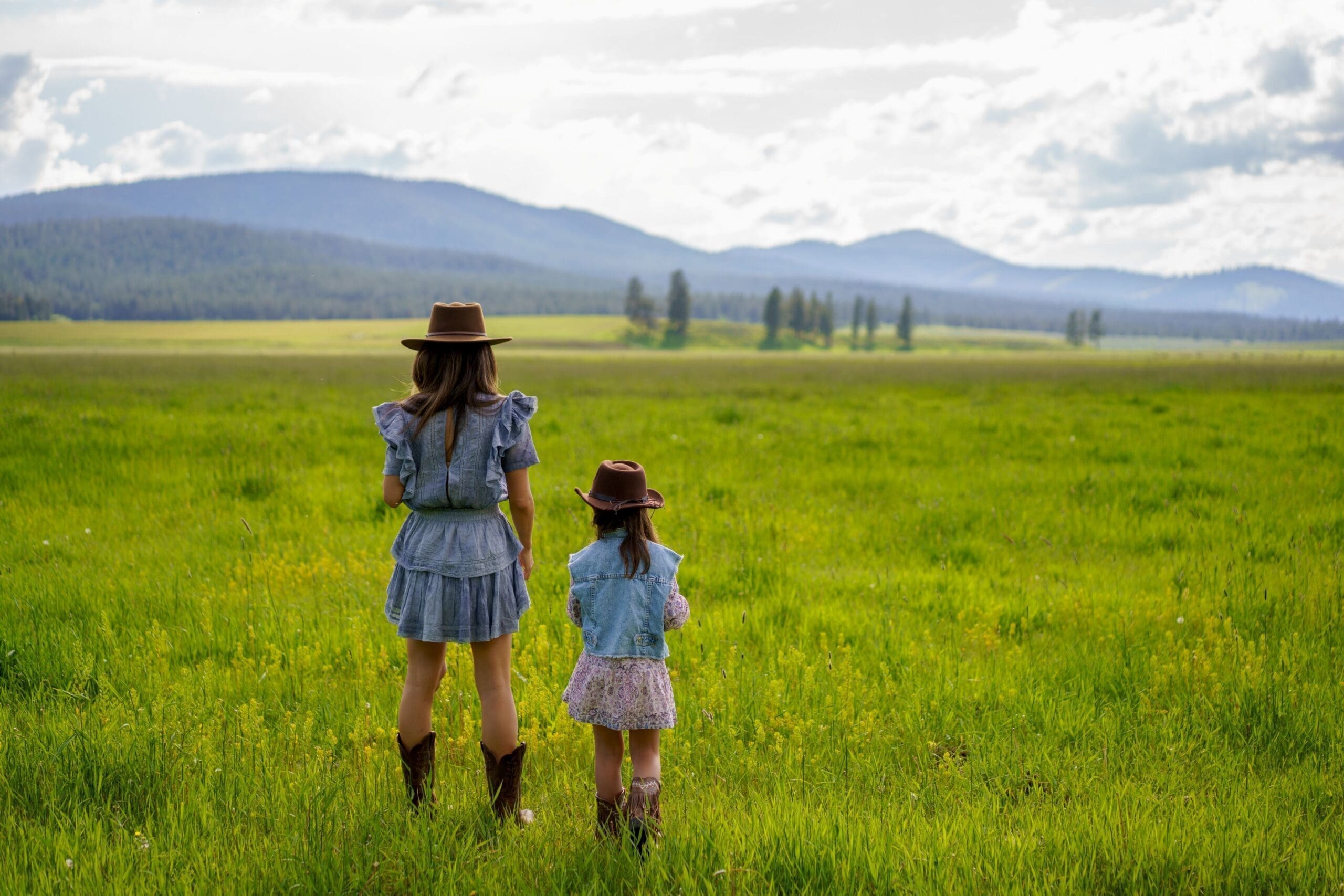 A mother and daughter standing in a summer mountain field wearing cowgirl hats