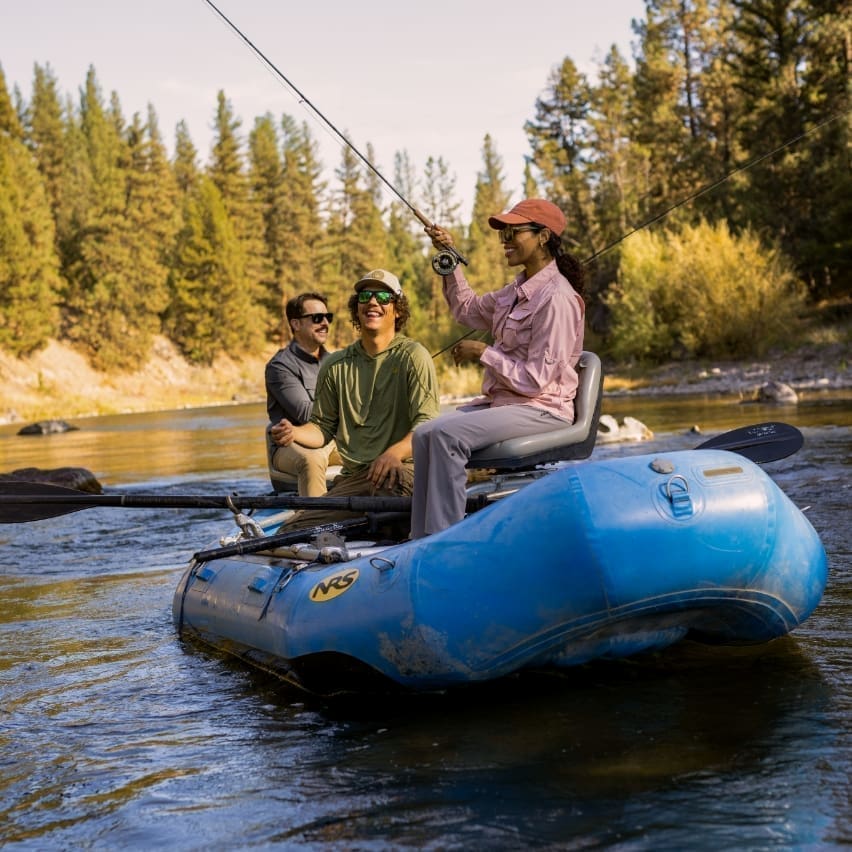 Group of people paddling a blue raft through the Blackfoot River to fly fish