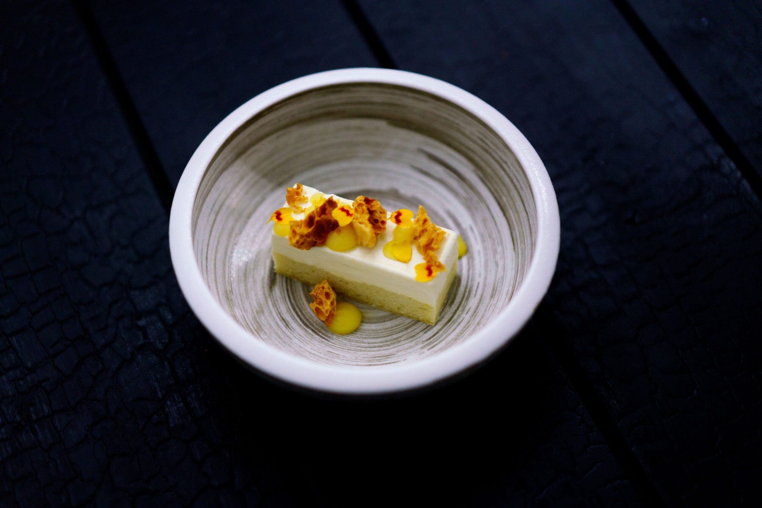 Clean slice of yellow cake with white frosting, decorated with flower petals and resting in a subtle gray bowl