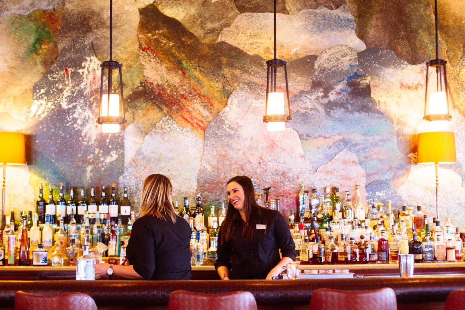 Two bartenders laughing behind the well-stocked bar, Tank, at Paws Up Montana