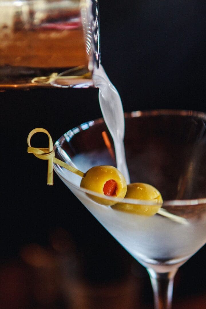 Shaker pouring a martini into a glass with two olives