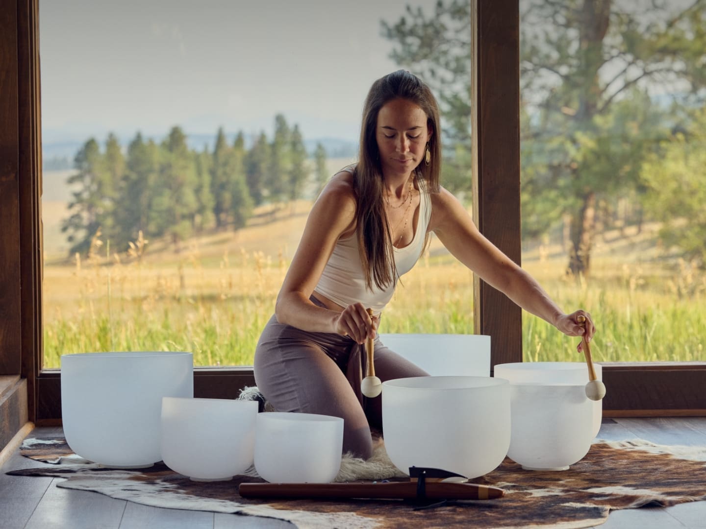 Female wellness instructor brushing sound bowls with mallets in yoga studio