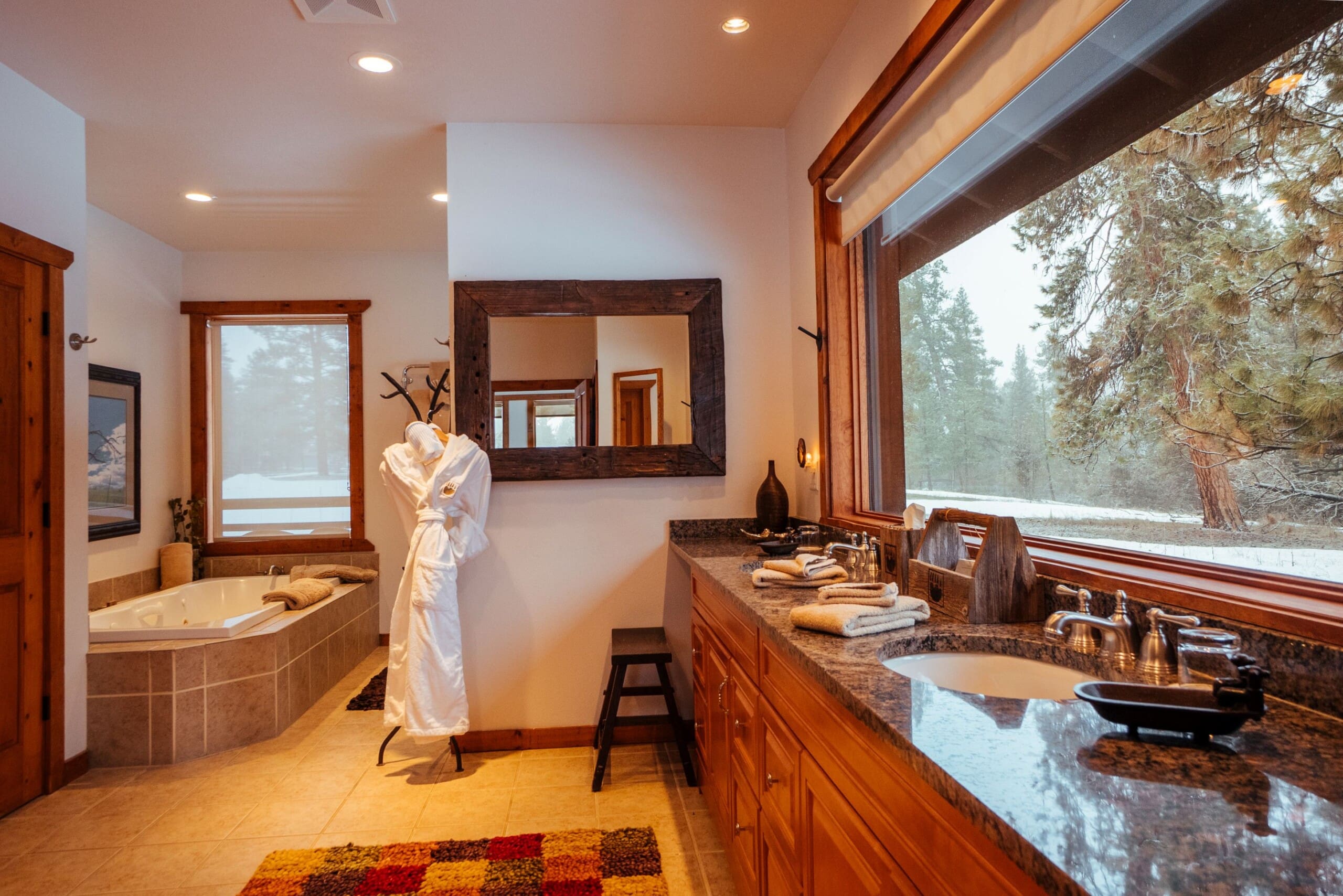 western style luxury bathroom with bathtub, sinks, and window with forest view