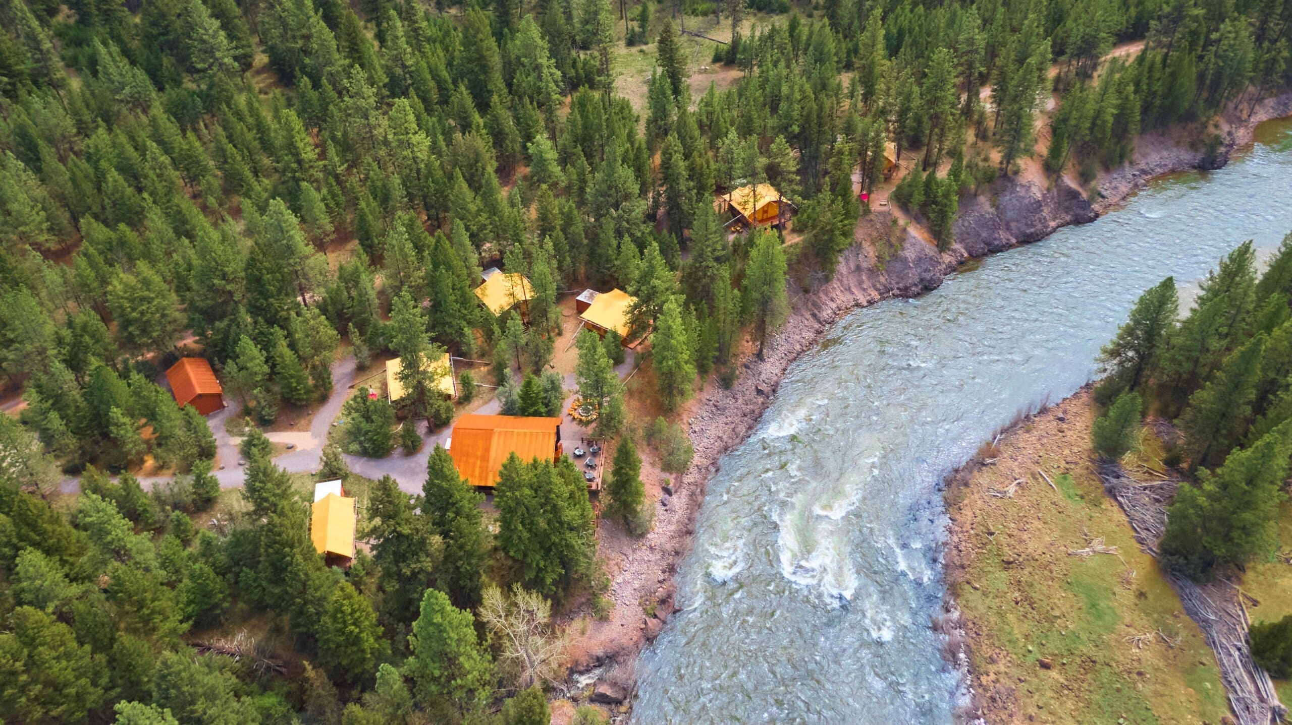 Aerial view of cliffside glamping camp by a river