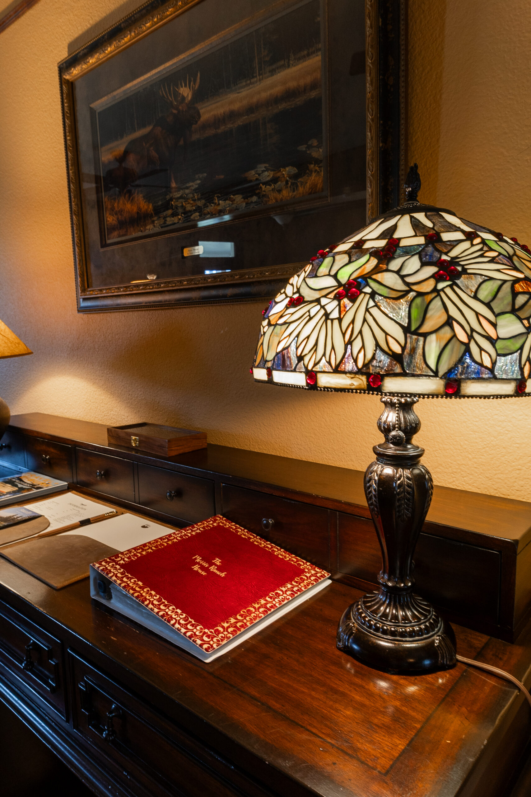 Multicolored lamp next to a red welcome book on a wooden table.