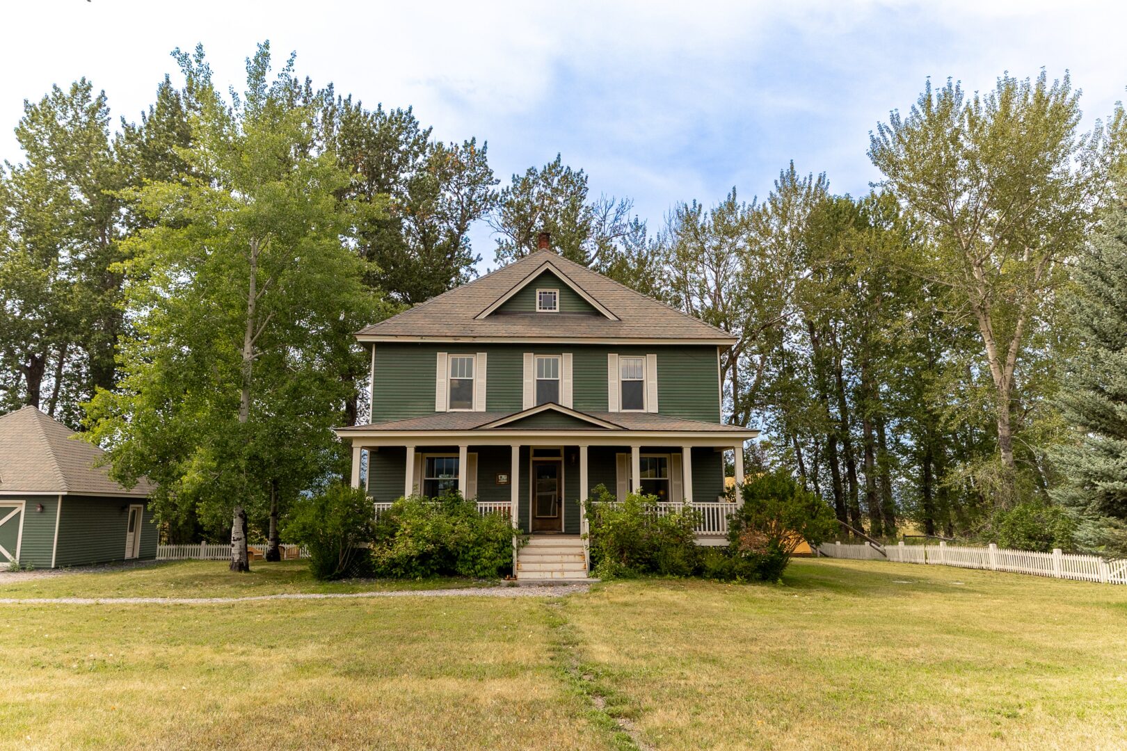 Green classic looking home with a large front yard and trees behind it.