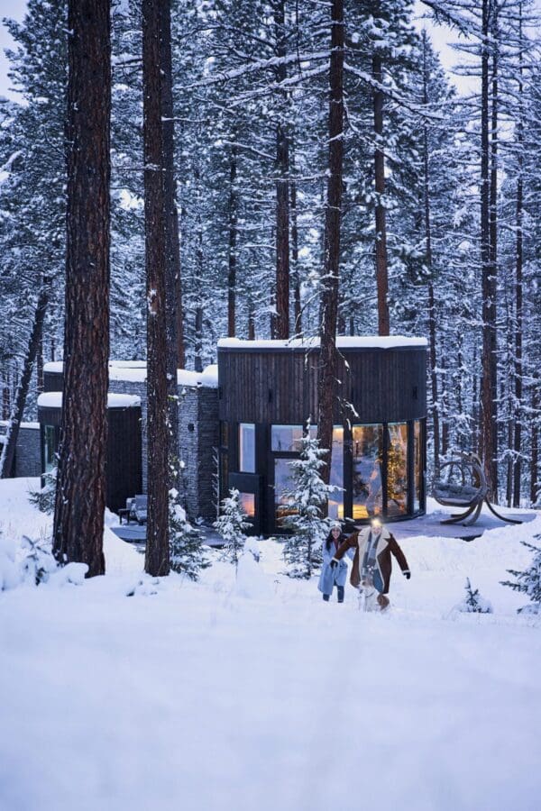 Couple walking through the snow with a cabin in the background.
