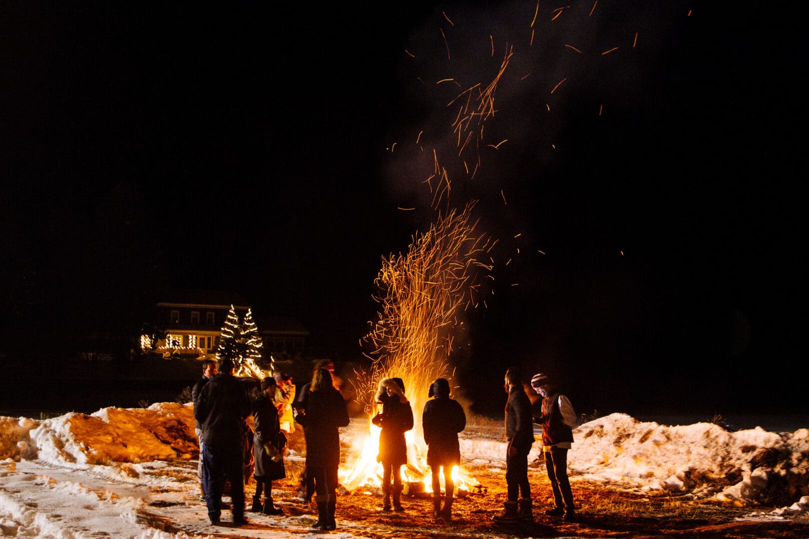 Group standing around a bonfire at night in the winter.