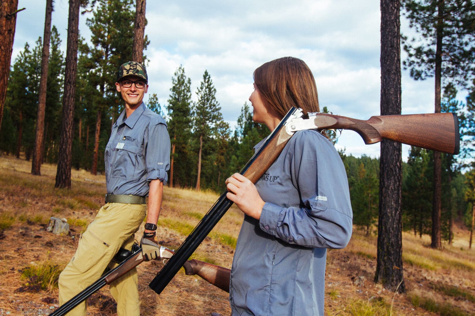 Two workers walking outside in the woods with an unloaded gun.
