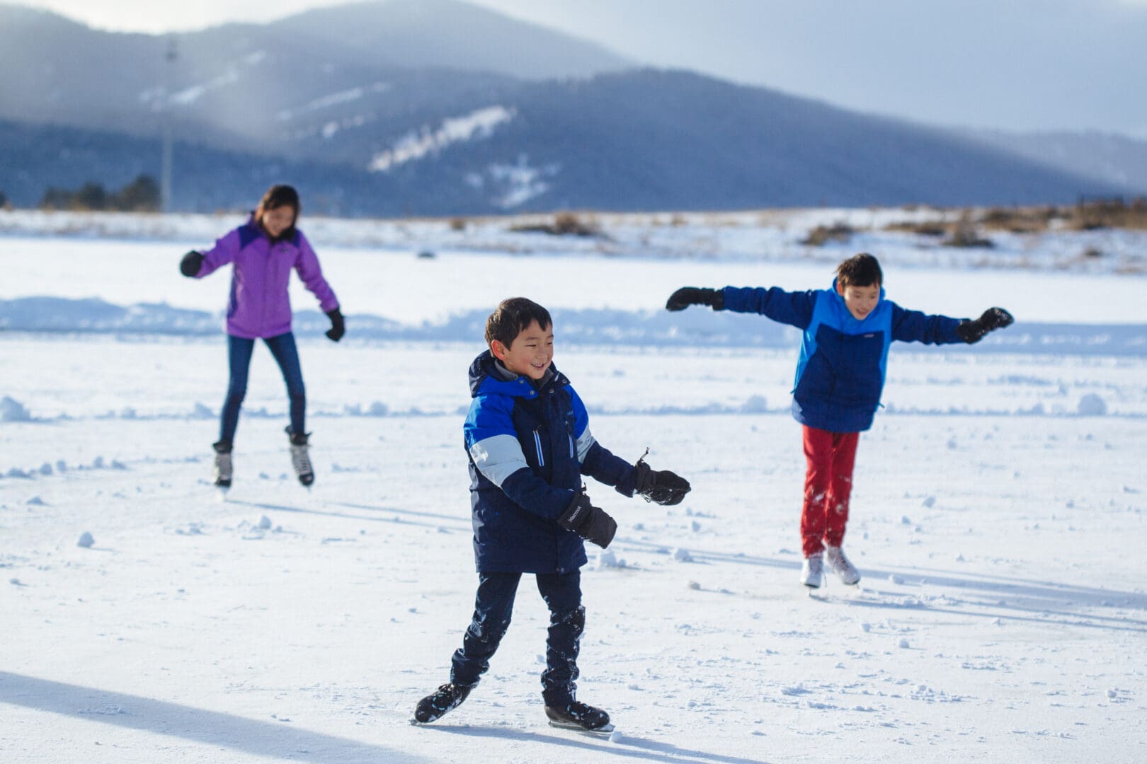 Three children ice skating during the winter time.
