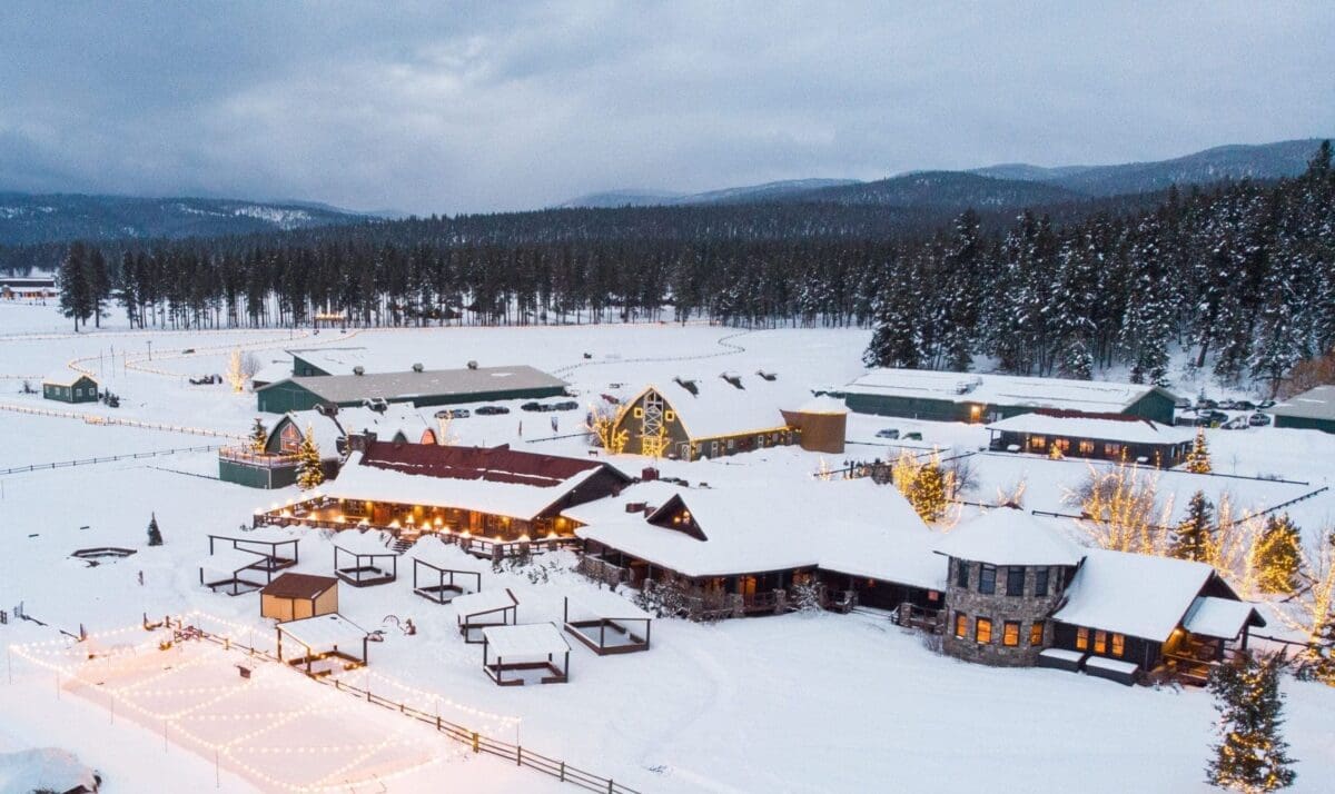 Overview shot of Paws Up Montana. The resort is covered in snow with glowy lights and a forest in the background.