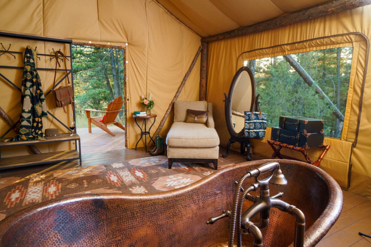 Cotton tub inside of a glamping tent with a chair, mirror, large windows, and open door.