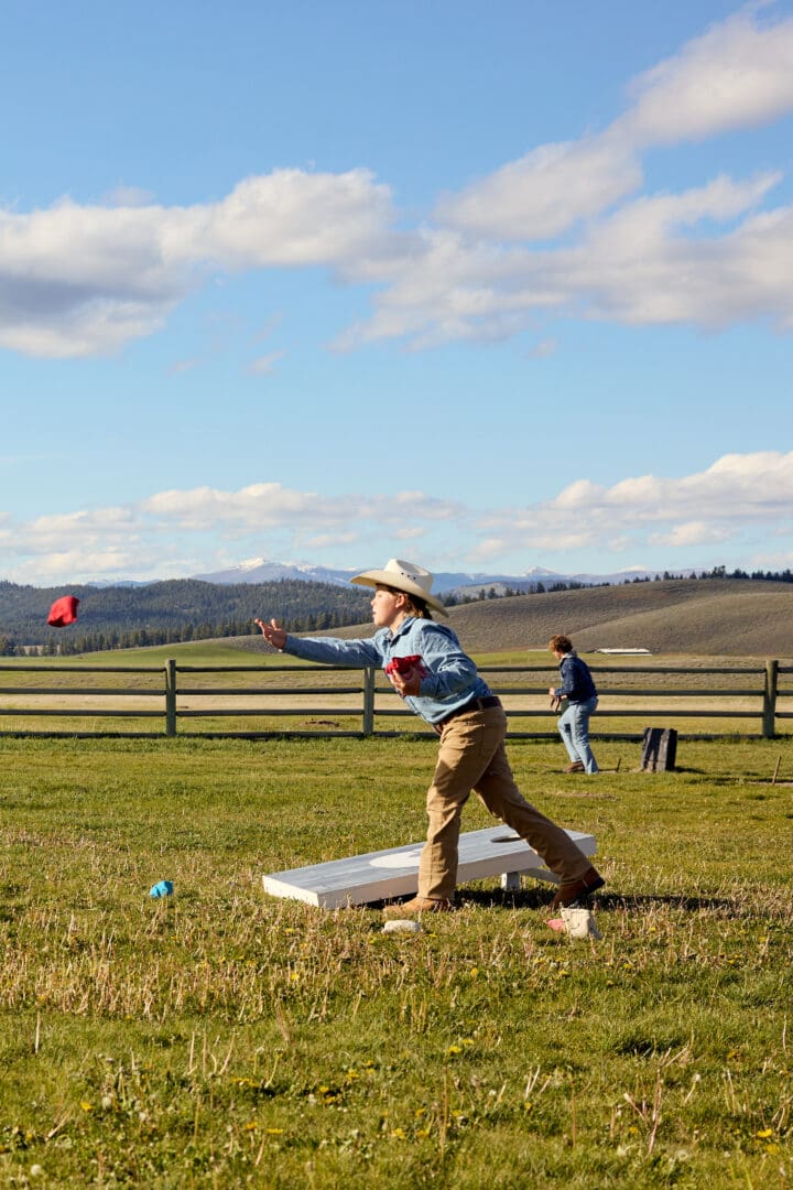Boy in a cowboy hat playing cornhole outside.