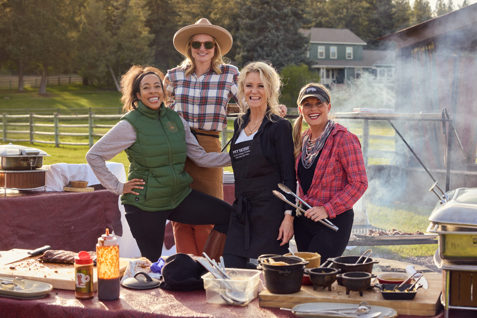 Four women outside grilling with an array of food in front of them on a table.