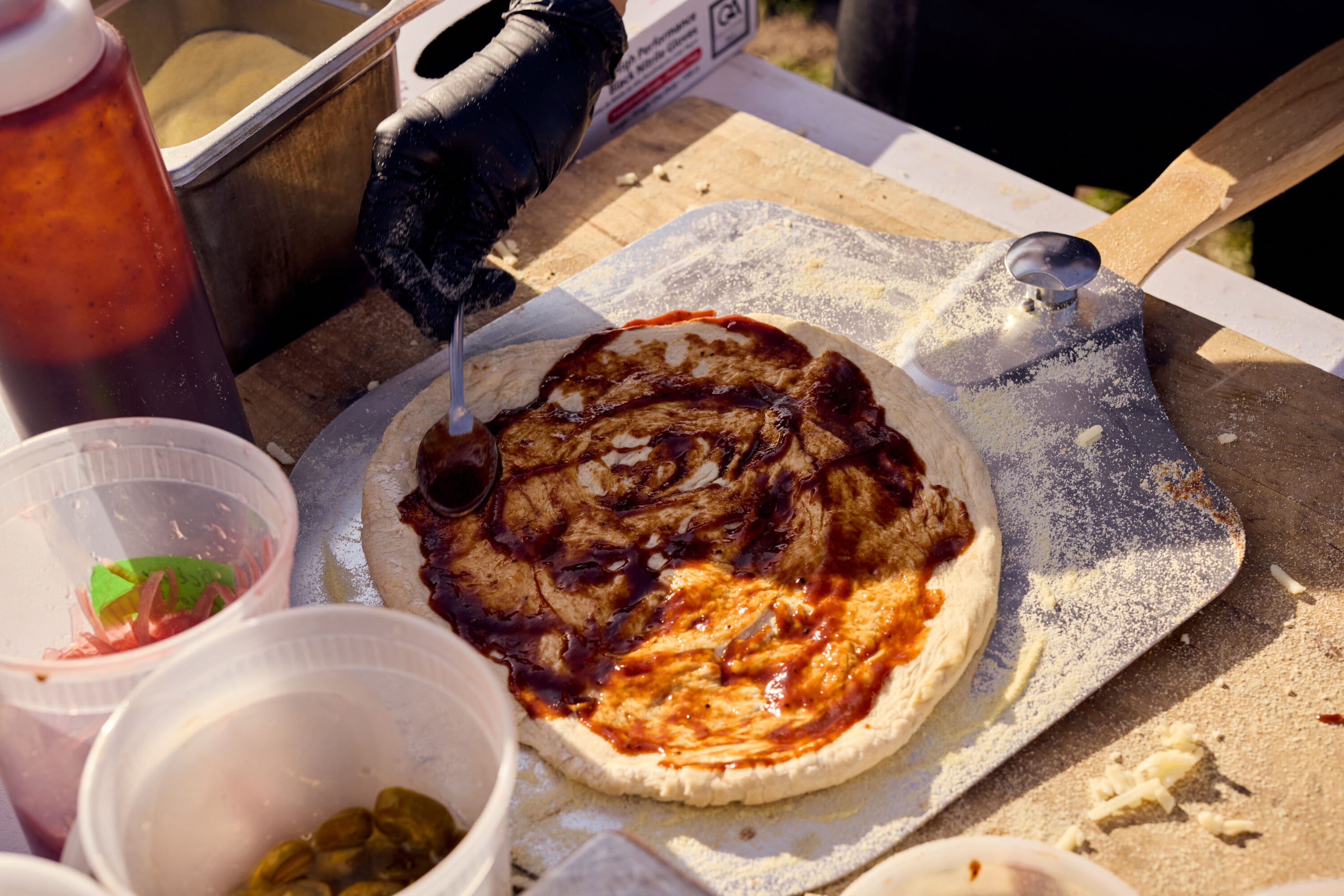 Pizza dough on a table with sauce being applied.