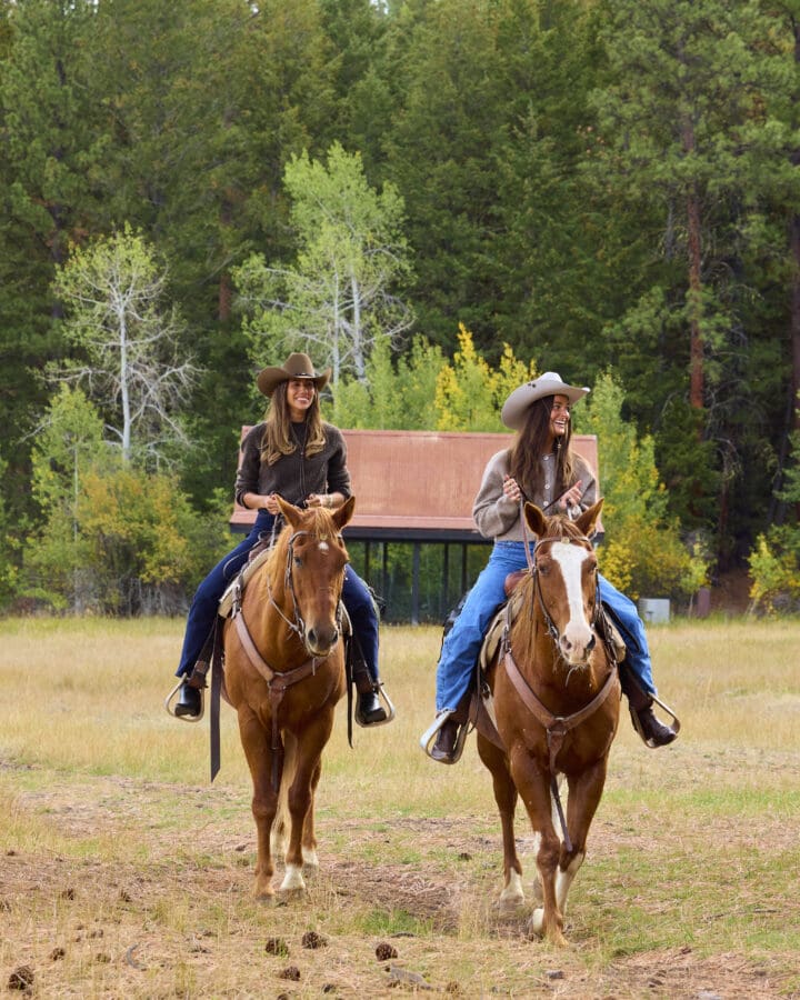 Two women riding horses outdoors.