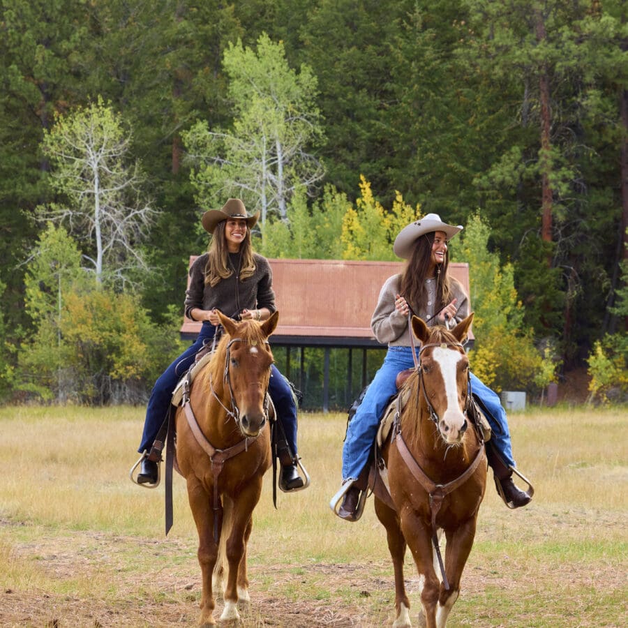 Two women riding horses outdoors.