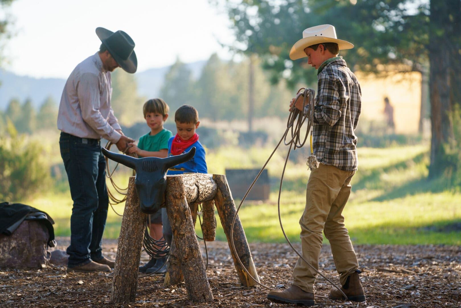 Man teaching a kid how to wrangle cattle with a fake wooden cattle and rope.