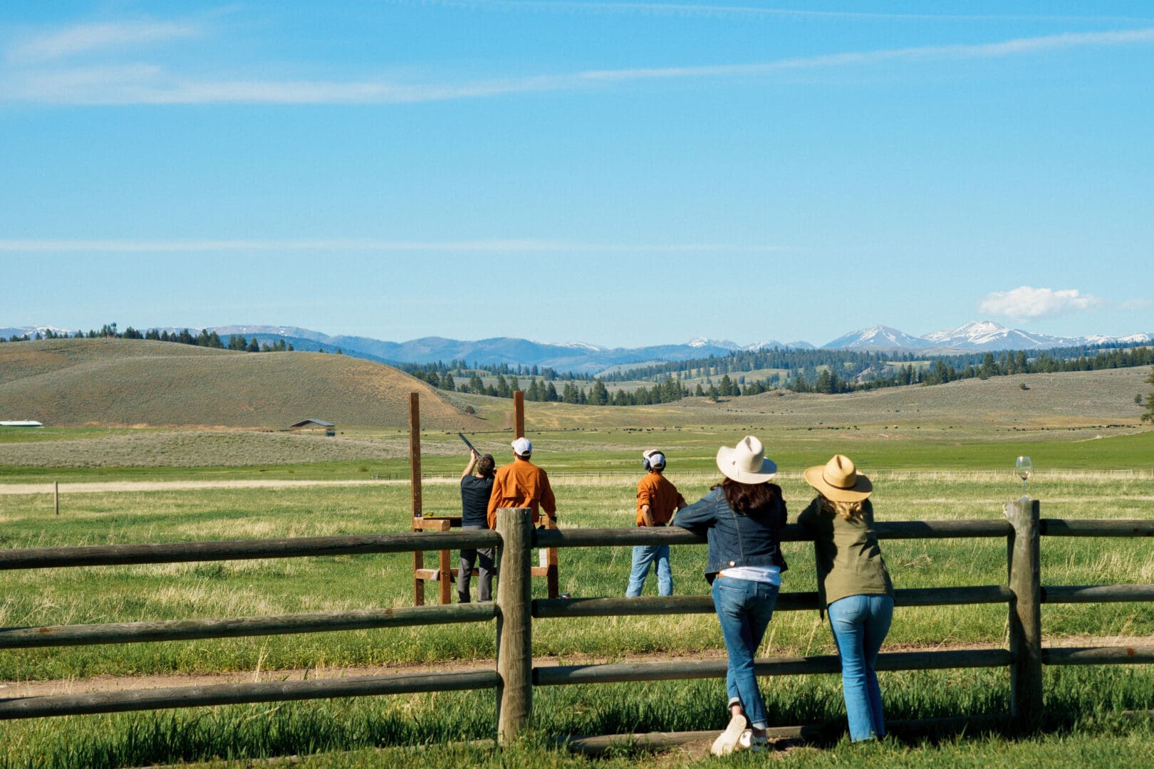 Group of people standing outside by a wooden fence looking out at a green field.