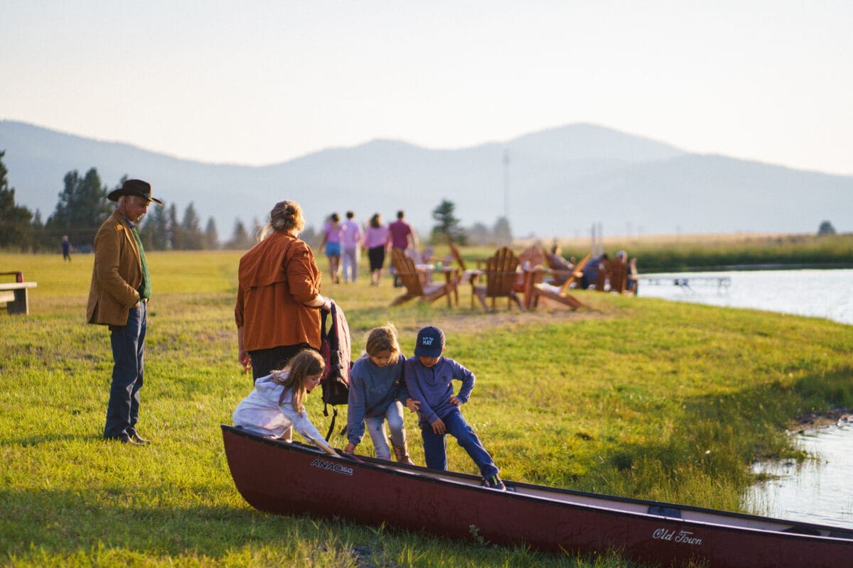 An older man and woman watching children play in a canoe.