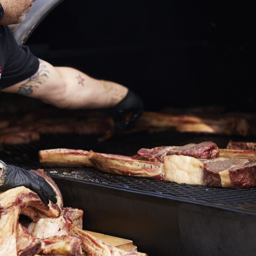 Arms reaching into a giant outdoor oven grilling meat.