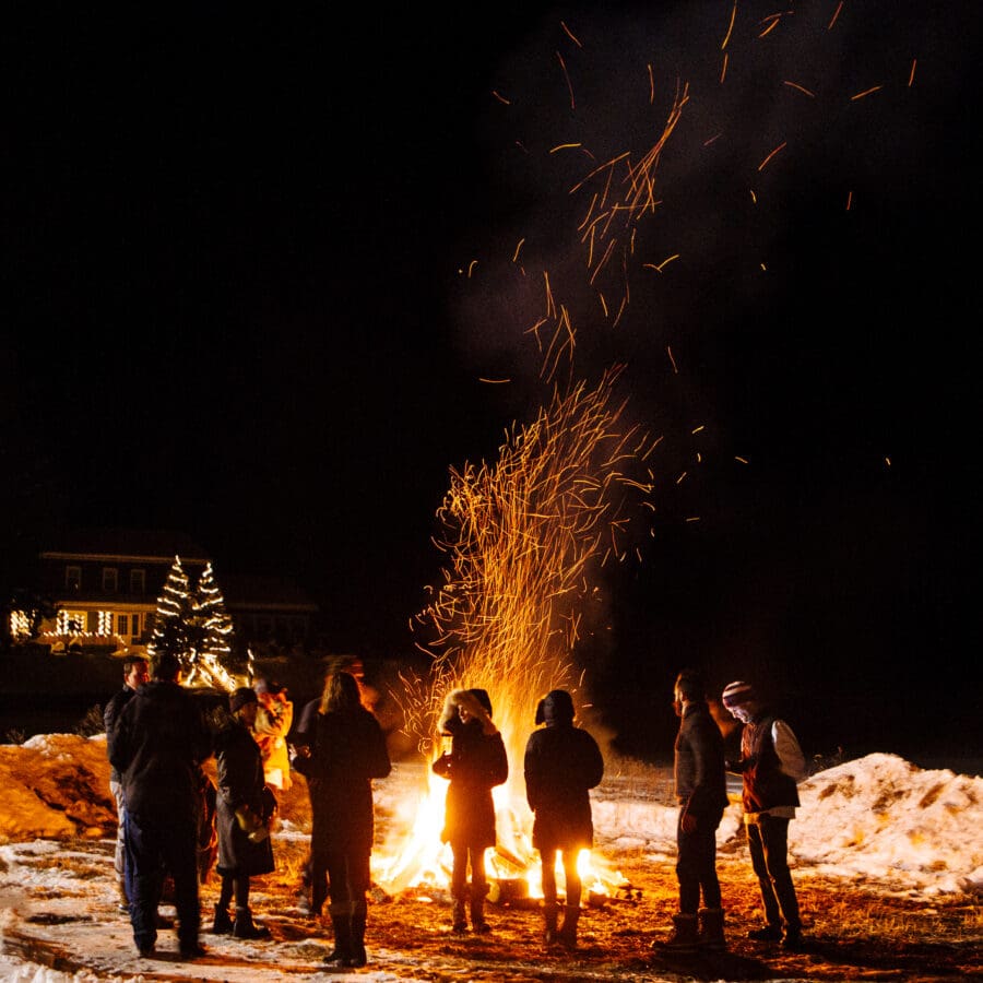 Group of individuals standing outside at night in the winter in front of a bonfire.