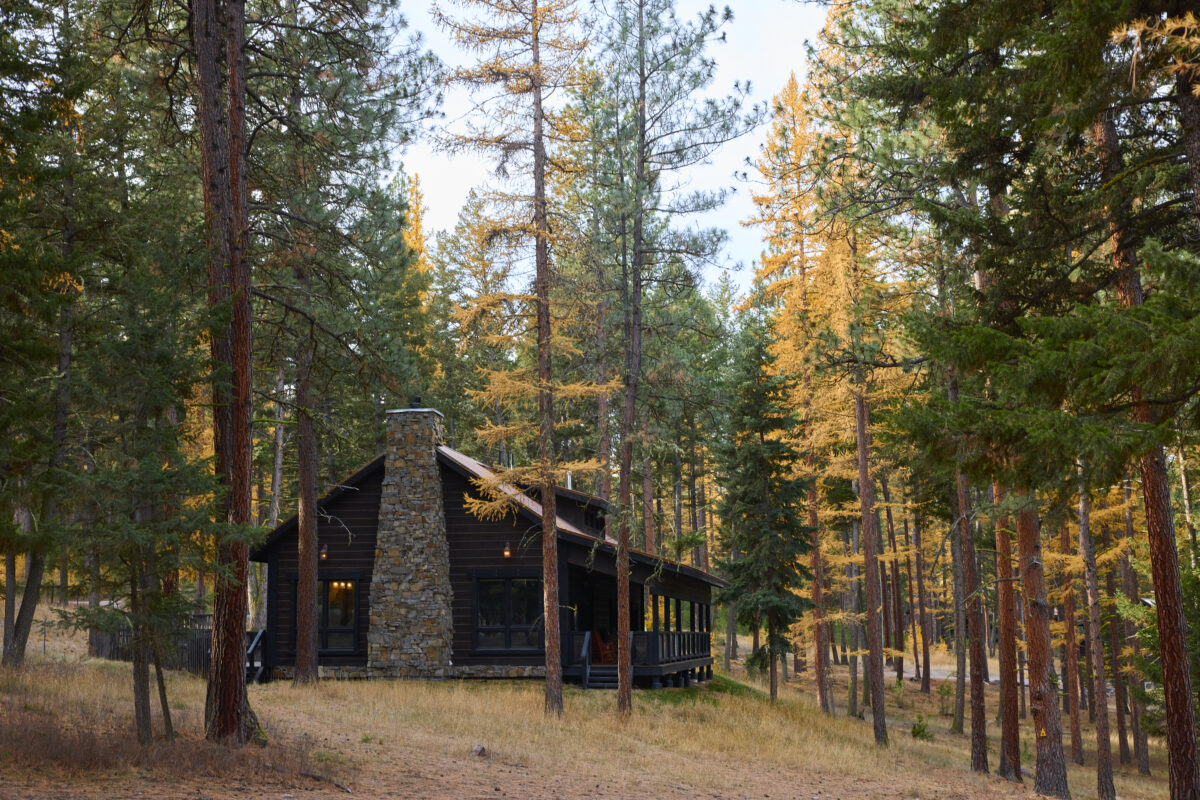 Wooden cabin surrounded by fall foliage trees and pines.