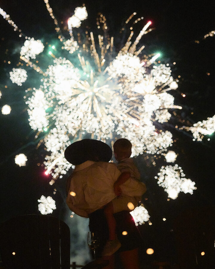 Mother holding her child at night with fireworks in the background.