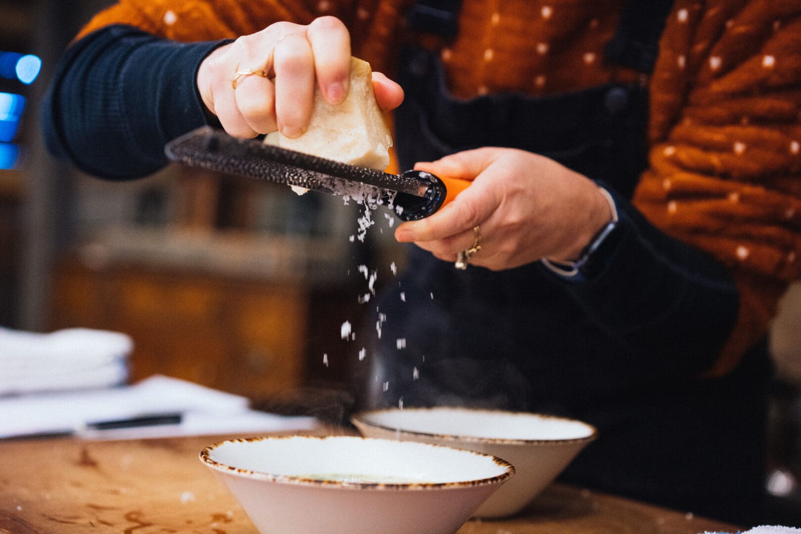 Shot of chefs hands as they are grating cheese over a dish in a bowl.