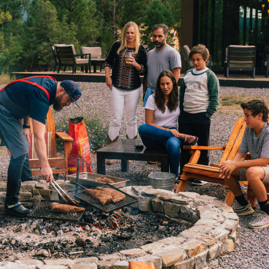 Worker cooking things over a fire while a family sits and watches.