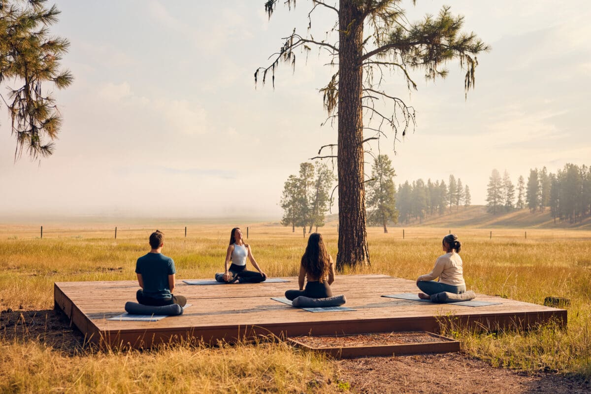 Fall wellness shot of people doing yoga and meditating outside with morning fog in the background.