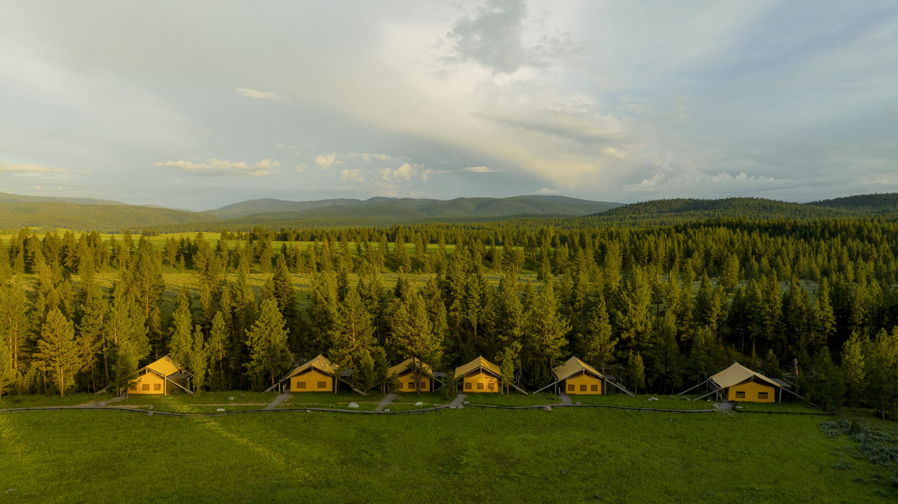 Series of tents lined up for an aerial shot with trees and mountains behind them.