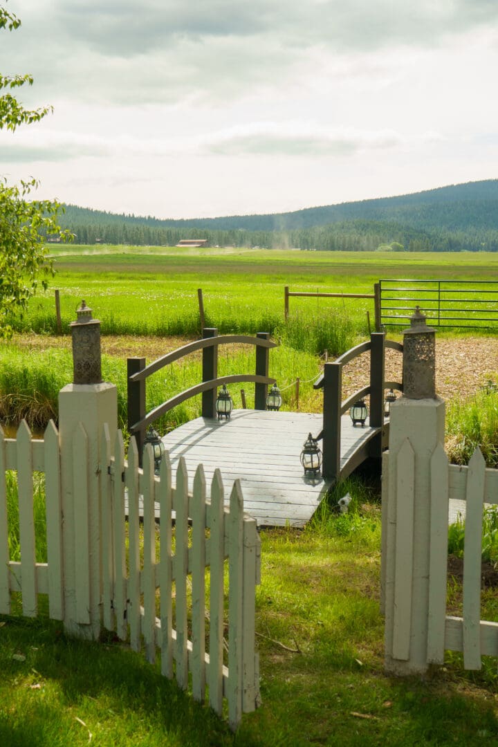 Green lawn with a white fence opening to a mini wooden bridge leading to the green yard.