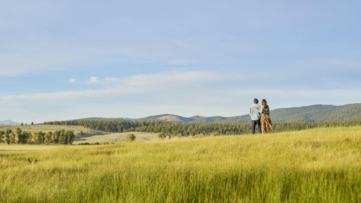 Couple standing in a field, overlooking mountains in the distance.
