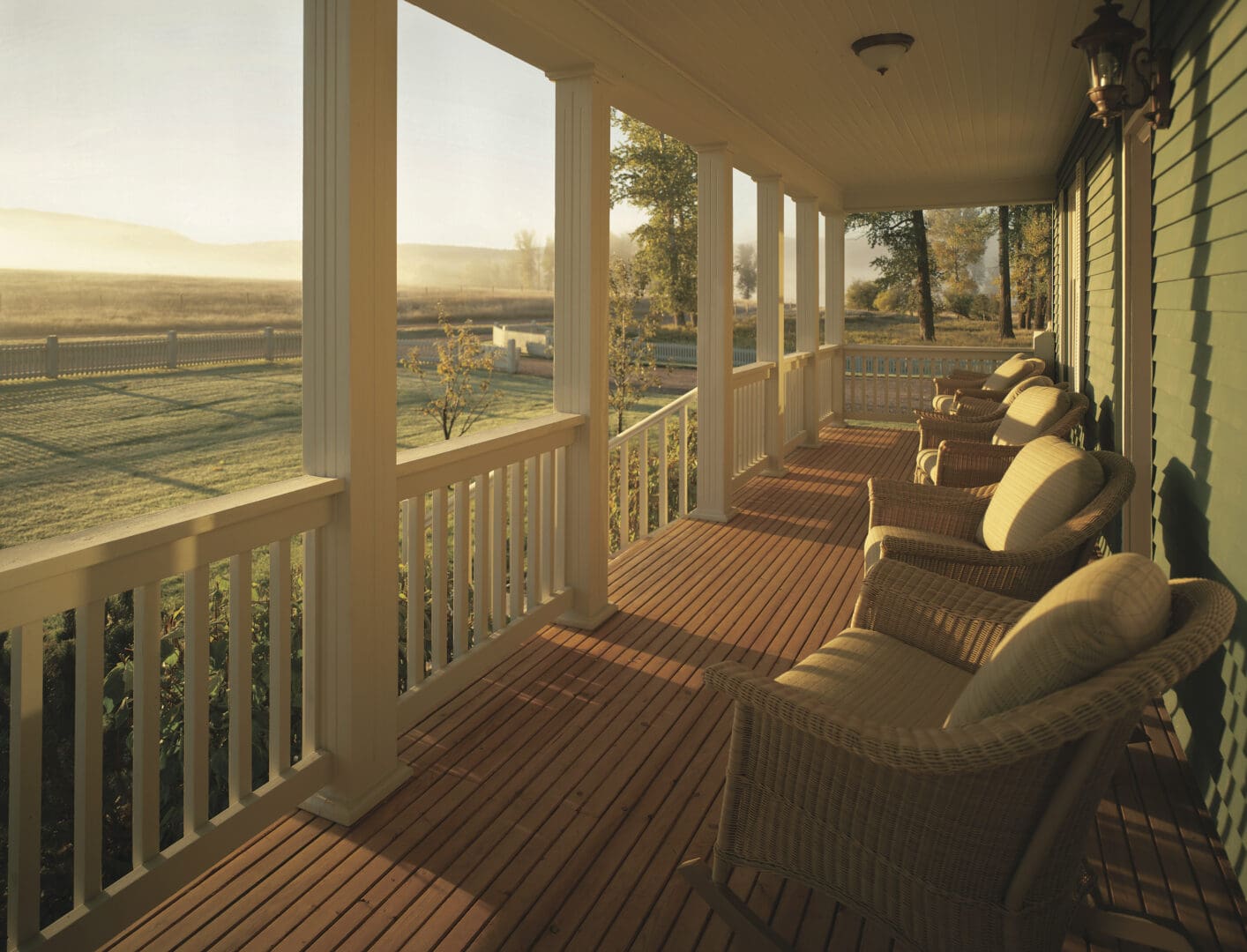 Long porch with chairs overlooking a green prairie at sunset.