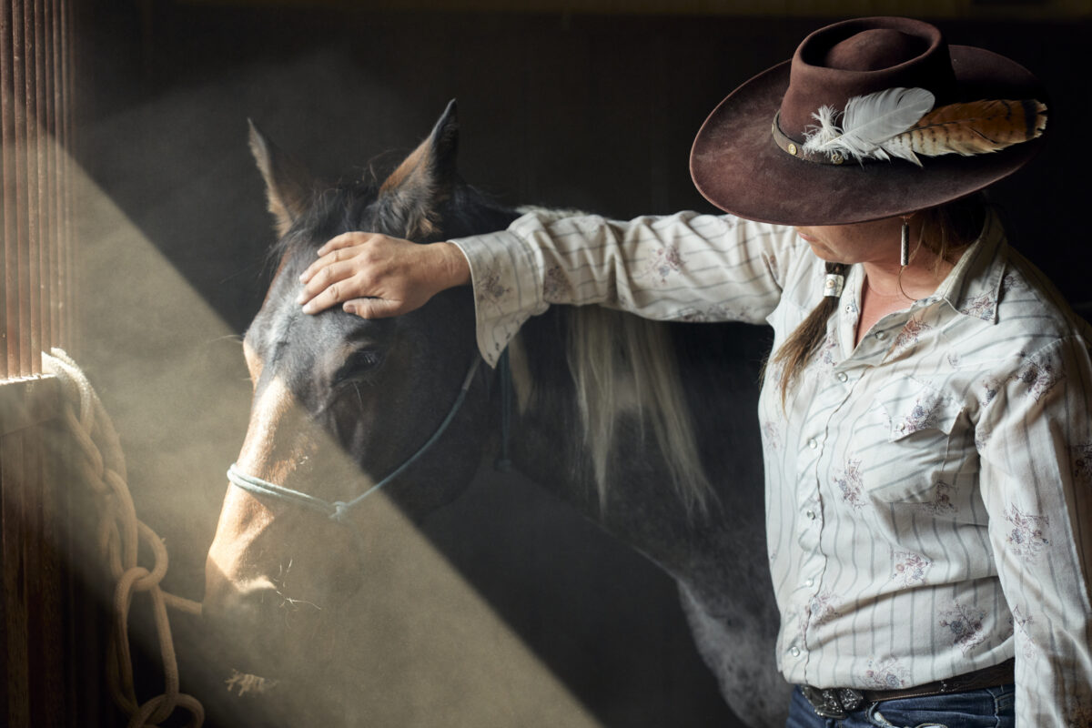 A Paws Up Montana horse trainer petting a horse in a dimly light barn.