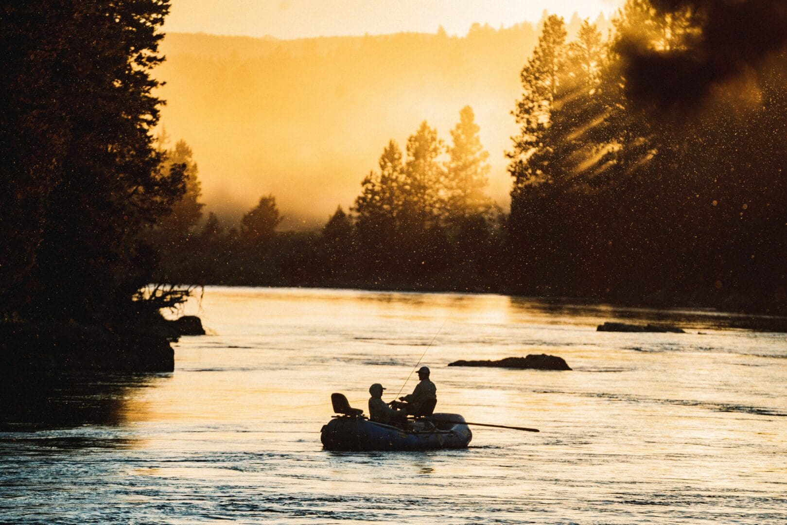 Two people on a boat with an orange sunset in the background on a river.