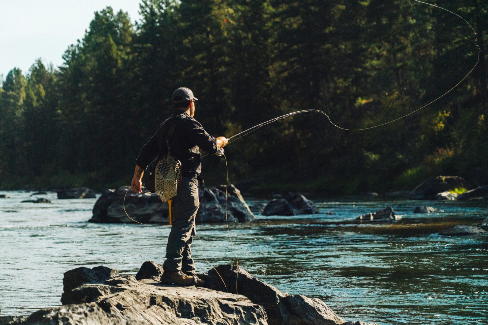 Man standing on the shore of a river fly fishing.