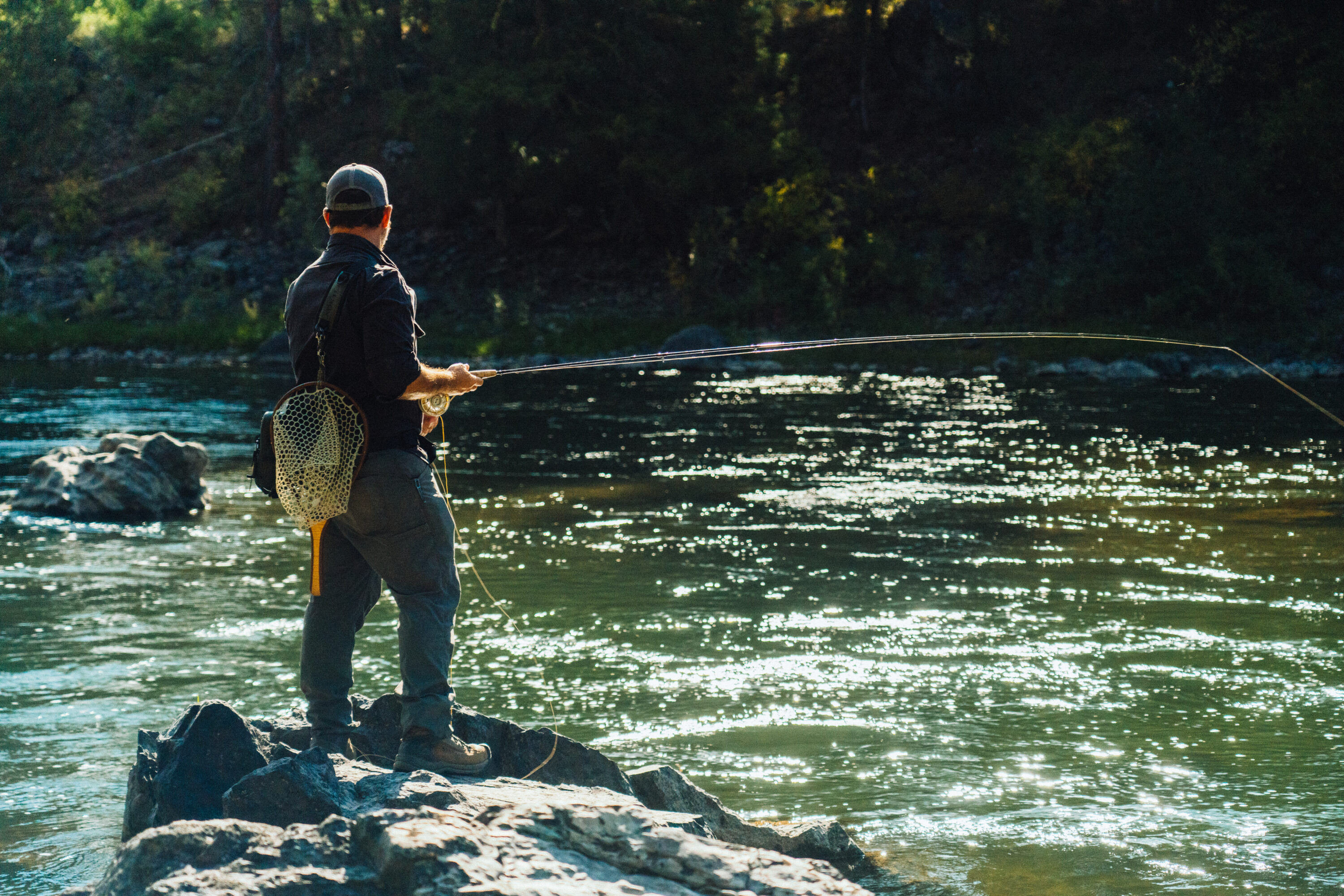 Man standing on the shore of a river fly fishing.