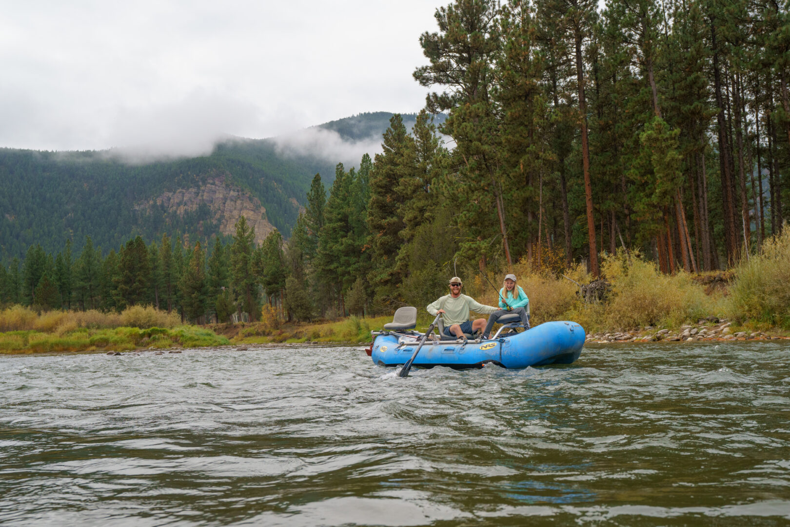 Man and young girl fishing in a blue boat with trees behind them in the distance.