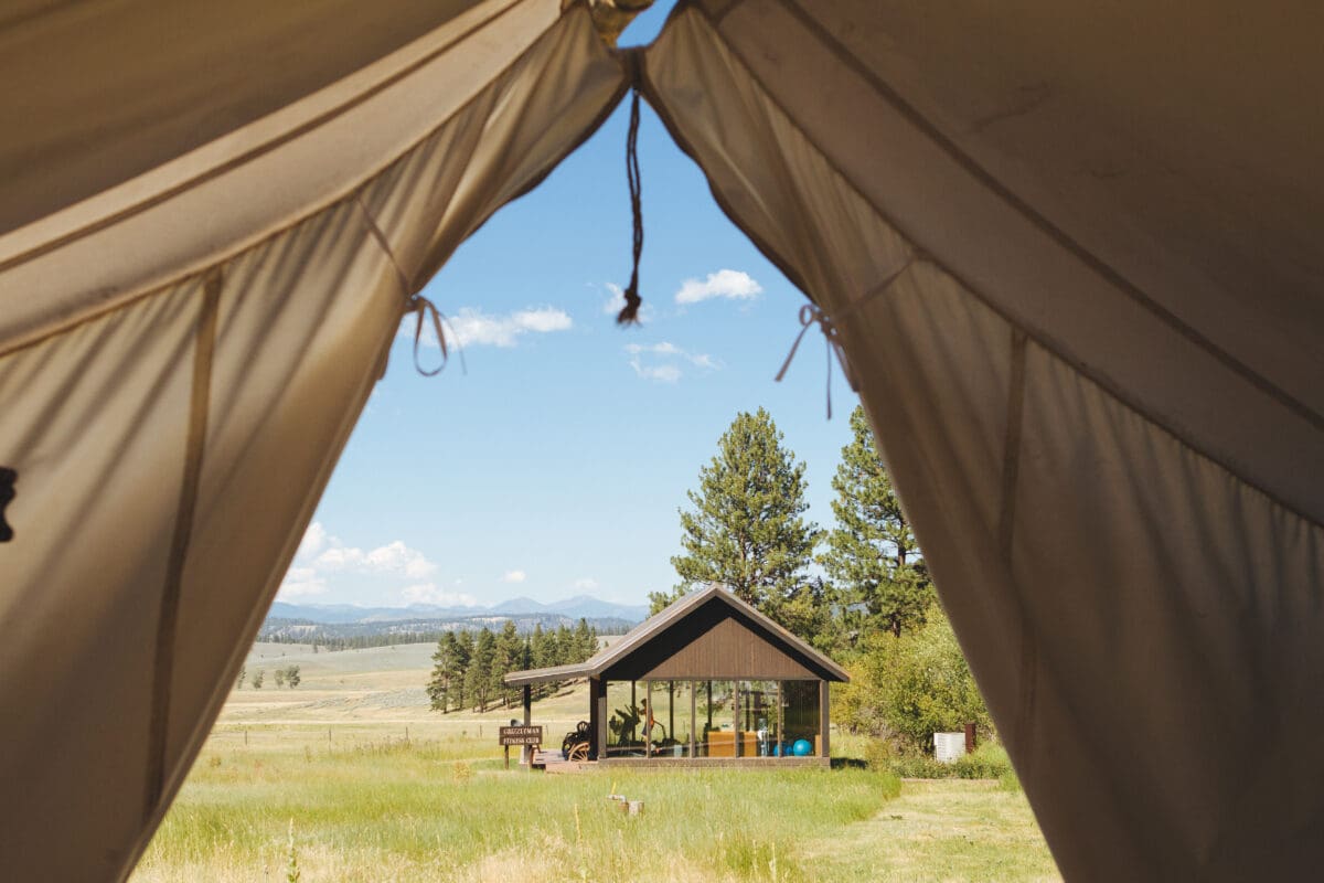 Spa tent with a view of a glass and wooden building on grass plains.