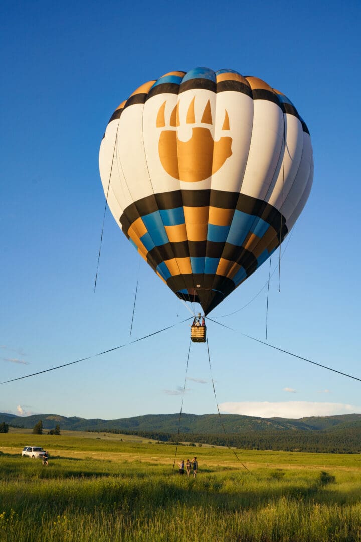 Hot air balloon tethered and floating in the sky with mountains and fields behind it.