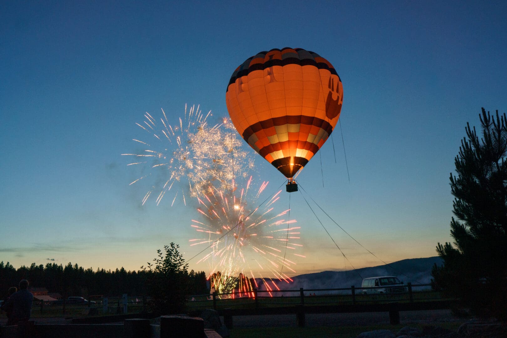 Hot air balloon in the sky with fireworks behind it.